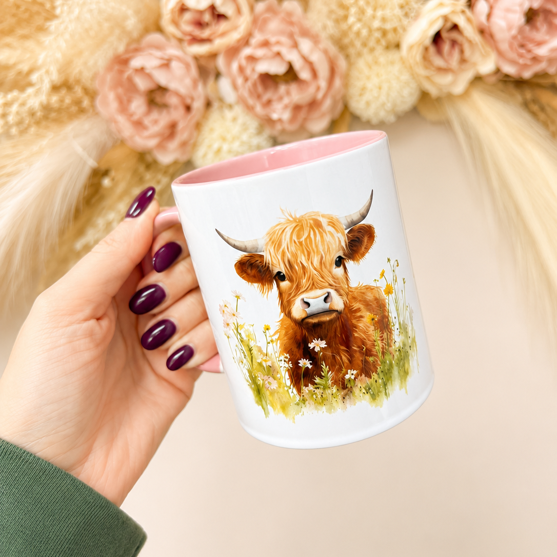 Hand holding a mug with a cow design in front of floral decorations