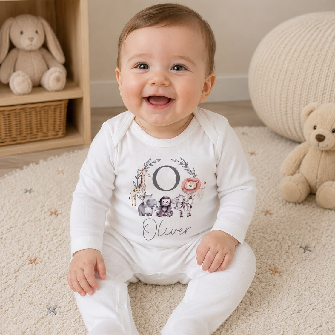 Baby wearing a white onesie with a floral design and text, sitting on a carpeted floor with toys around.