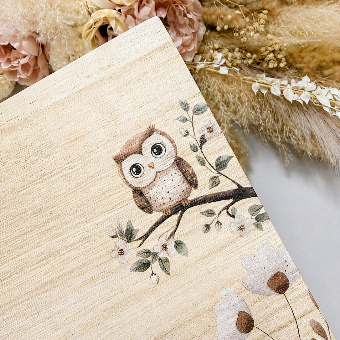 Wooden block with an owl design on a decorative background with flowers and leaves.