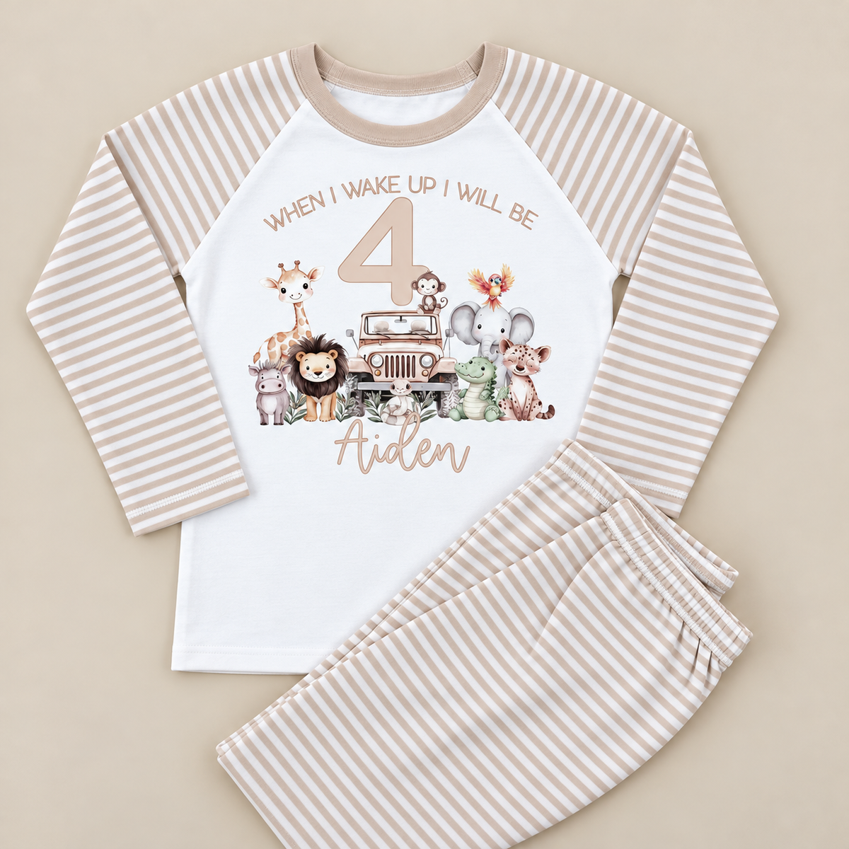 A two-piece children's pajama set laid flat on a light beige background. The long-sleeve top is white with beige and taupe vertical stripes on the sleeves and collar, featuring a safari-themed 4th birthday graphic with cartoon animals and the text 'When I wake up I will be 4' and 'Aiden'.