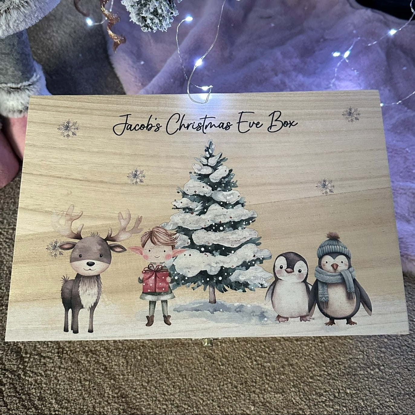 Wooden Christmas Eve box with festive design featuring a tree, deer, and penguins on a textured surface.