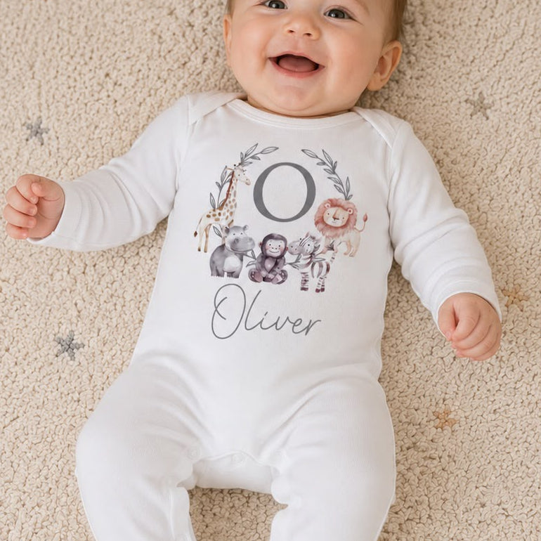 Baby wearing a white onesie with 'Oliver' printed on it, lying on a carpeted floor.