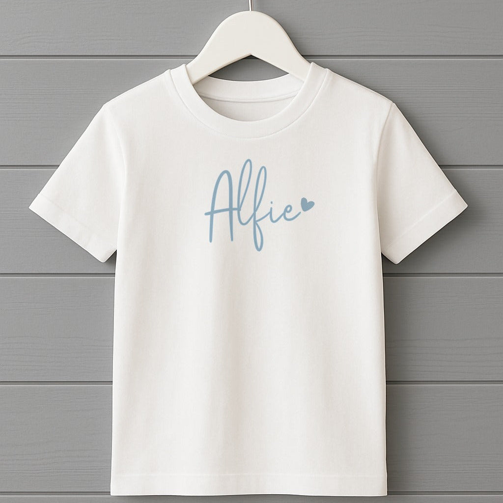White t-shirt with 'Alfie' printed on it hanging on a gray wooden background