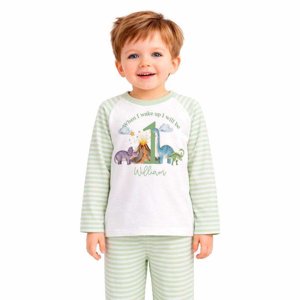 Child wearing a green and white striped pajama set with dinosaur design on a white background